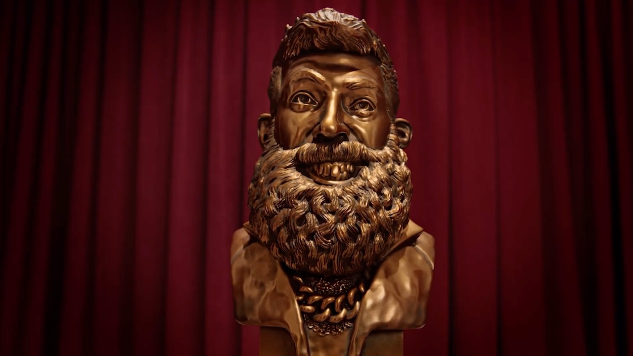 Bronze bust statue on a red velvet stage, from the State Farm 'Bundle Bust' campaign featuring Ryan Fitzpatrick and Charissa Thompson.