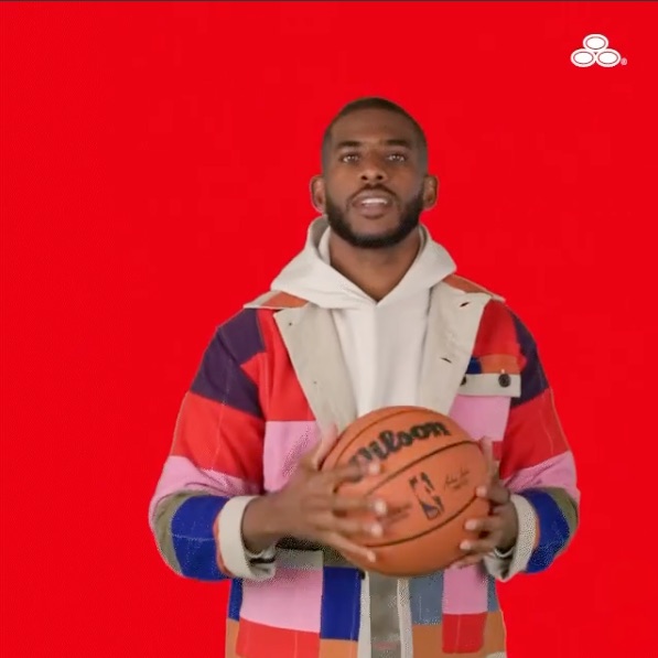 Chris Paul holding a basketball on a State Farm red backdrop.