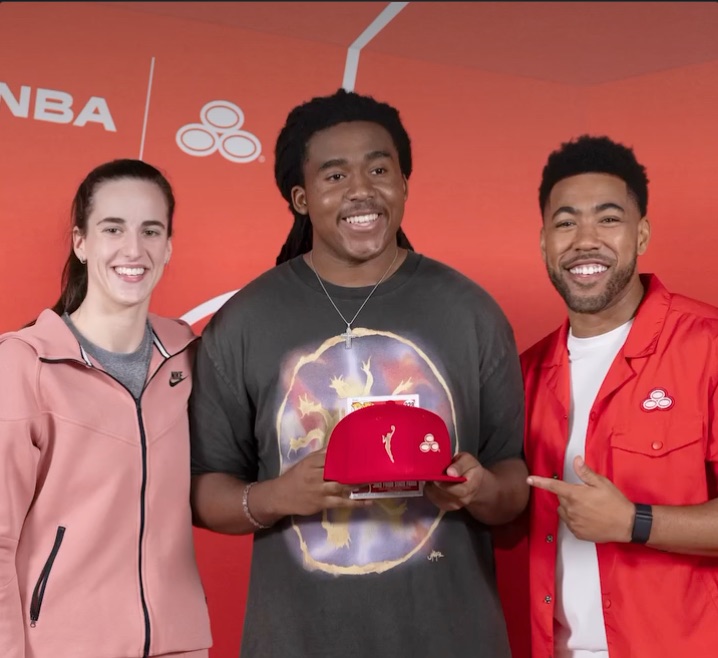 Caitlin Clark and two others holding a red WNBA × State Farm cap.